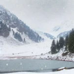 A realistic winter photograph inspired by Ratti Gali Lake in Pakistan, with snowfall covering the landscape. The scene shows the alpine lake surrounde